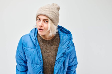 Téléchargez les photos : Femme en tenue d'hiver avec bonnet et veste en peluche bleue regardant loin sur un fond uni. - en image libre de droit