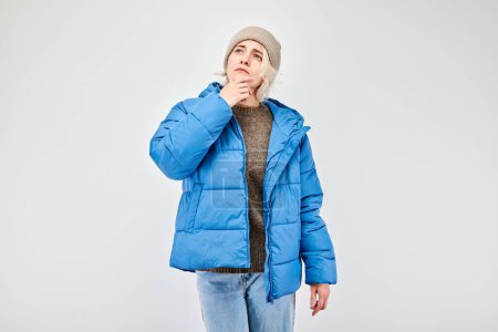 Photo for Woman in winter attire with pensive expression, thinks, chooses isolated on light background - Royalty Free Image