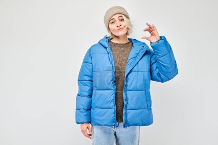 Téléchargez les photos : Femme en veste d'hiver bleue gestuelle petite quantité avec les doigts, isolée sur fond clair. - en image libre de droit