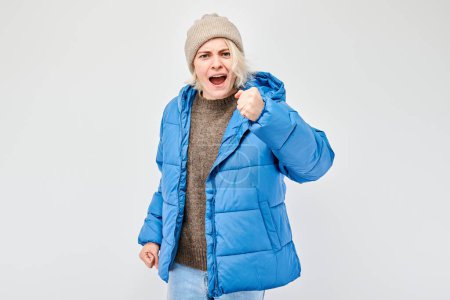 Woman in winter attire screams with anger against a white background.