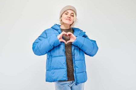 Photo for Woman in blue winter jacket making heart shape with hands, isolated on light background. - Royalty Free Image