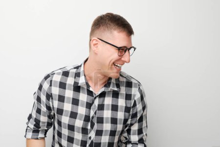 Foto de Joven alegre en gafas y camisa a cuadros riendo sobre un fondo blanco. - Imagen libre de derechos