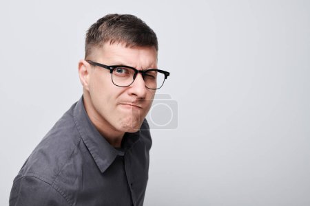 Téléchargez les photos : Jeune homme confus avec des lunettes qui plissent et froncent les sourcils sur un fond gris. - en image libre de droit