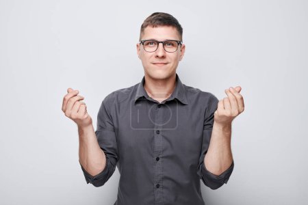 Foto de Hombre seguro en gafas y camisa haciendo gesto esperanzador con los dedos cruzados sobre fondo claro. - Imagen libre de derechos