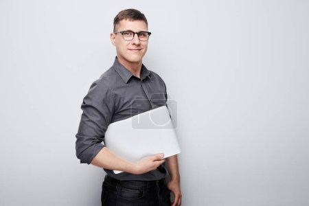Foto de Joven confiado en gafas que sostienen un portátil sobre un fondo blanco con espacio para copiar. - Imagen libre de derechos