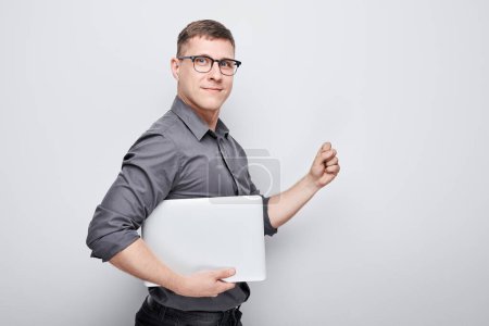 Téléchargez les photos : Joyeux homme d'affaires gestionnaire programmeur tient un ordinateur portable dans ses mains et sourit sur un fond blanc. - en image libre de droit