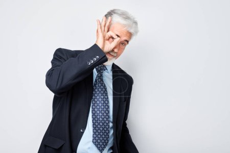 Téléchargez les photos : Homme d'affaires senior faisant un geste OK avec main sur œil, isolé sur fond blanc. - en image libre de droit