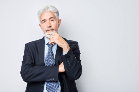 Photo for Confident senior businessman in suit, pondering with hand on chin, isolated on grey background. - Royalty Free Image