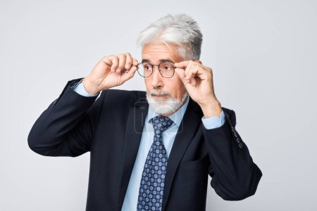 Téléchargez les photos : Homme d'affaires senior confiant ajustant ses lunettes, isolé sur fond gris. - en image libre de droit