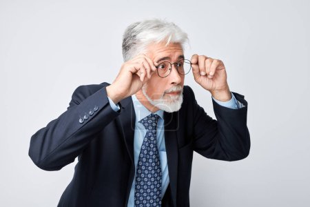Téléchargez les photos : Homme d'affaires senior confiant ajustant ses lunettes, isolé sur fond gris. - en image libre de droit