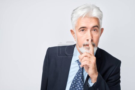 Foto de Hombre de negocios maduro con pelo gris haciendo gestos de silencio con el dedo en los labios aislados sobre fondo gris - Imagen libre de derechos