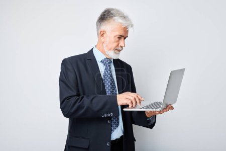 Téléchargez les photos : Homme d'affaires senior utilisant un ordinateur portable sur fond blanc. - en image libre de droit