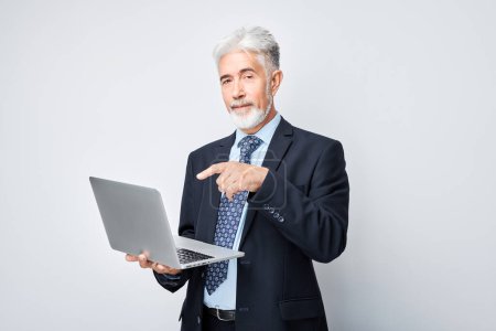 Foto de Hombre de negocios senior usando el ordenador portátil en el fondo blanco, señala con un dedo a la pantalla - Imagen libre de derechos