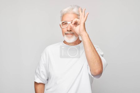 Photo for Senior man with glasses making OK gesture on a gray background. - Royalty Free Image