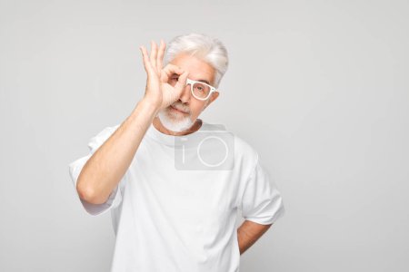 Photo for Senior man with glasses making OK gesture on a gray background. - Royalty Free Image