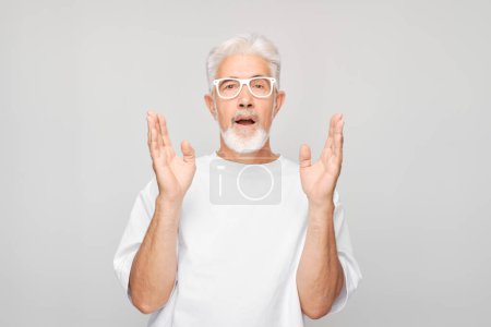 Foto de Hombre mayor con gafas haciendo un gesto sorprendido, aislado sobre un fondo gris. - Imagen libre de derechos