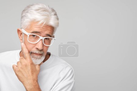 Téléchargez les photos : Homme âgé aux cheveux blancs et lunettes à la recherche réfléchie, isolé sur un fond gris. - en image libre de droit