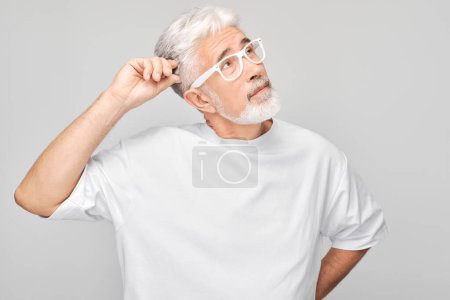 Téléchargez les photos : Homme mûr avec des cheveux blancs et des lunettes à la recherche réfléchie sur un fond gris. - en image libre de droit