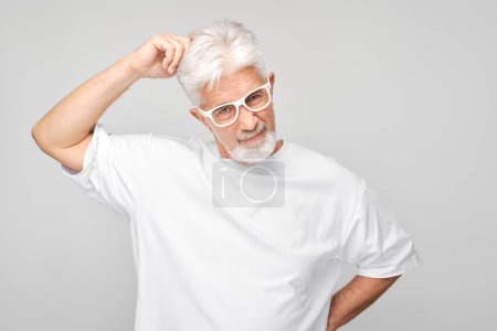 Téléchargez les photos : Homme mûr avec des cheveux blancs et des lunettes à la recherche réfléchie sur un fond gris. - en image libre de droit
