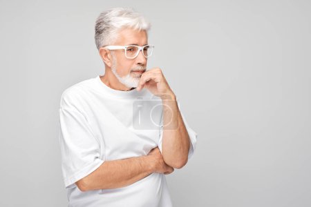 Téléchargez les photos : Homme âgé réfléchi avec des lunettes regardant loin sur un fond gris - en image libre de droit