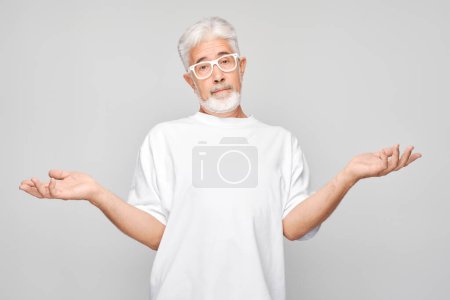 Photo for Confused senior man with glasses shrugging shoulders on a gray background. - Royalty Free Image