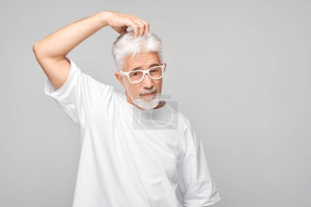 Téléchargez les photos : Homme âgé confiant avec des lunettes posant sur un fond gris. - en image libre de droit