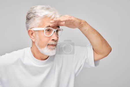 Téléchargez les photos : Homme âgé avec des cheveux blancs et des lunettes regardant au loin avec la main au-dessus des yeux, à la recherche - en image libre de droit