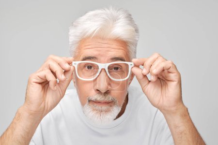 Téléchargez les photos : Homme âgé avec des lunettes de réglage des cheveux blancs regardant la caméra avec une expression curieuse - en image libre de droit