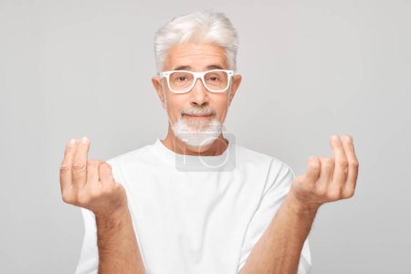 Téléchargez les photos : Homme âgé montrant des cœurs ou un signe d'argent avec un doigt sur fond blanc - en image libre de droit