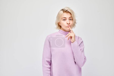 Foto de Mujer joven pensativa en un suéter púrpura, mano en la barbilla, mirando reflexivo sobre un fondo claro. - Imagen libre de derechos