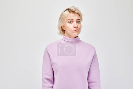 Téléchargez les photos : Jeune femme confus dans un pull violet, ce qui rend une expression perplexe sur un fond gris clair. - en image libre de droit
