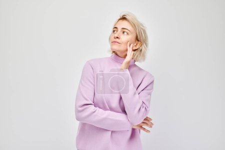 Thoughtful woman in a purple sweater looking upwards, isolated on a white background.