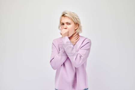 Retrato de una mujer rubia enferma tosiendo en el puño, el resfriado y la gripe