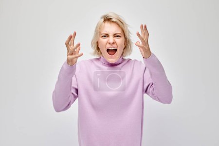 Téléchargez les photos : Femme en colère dans un pull violet serrant ses poings et criant, isolé sur un fond blanc. - en image libre de droit