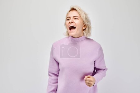 Foto de Mujer enojada en un suéter púrpura apretando los puños y gritando, aislada sobre un fondo blanco. - Imagen libre de derechos