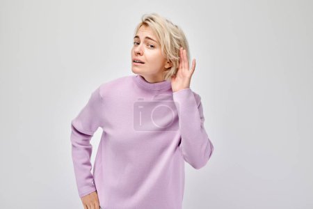 Téléchargez les photos : Femme en pull violet écoutant avec la main à l'oreille, fond blanc. - en image libre de droit