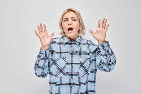 Photo for Surprised young woman with hands up and open mouth wearing a plaid shirt on a light background. - Royalty Free Image