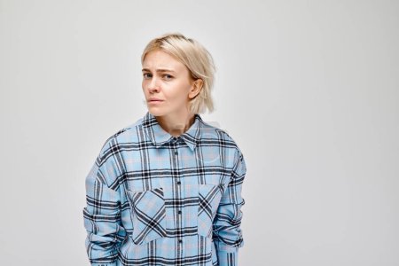 Téléchargez les photos : Jeune femme en chemise à carreaux regardant incertain sur un fond gris. - en image libre de droit