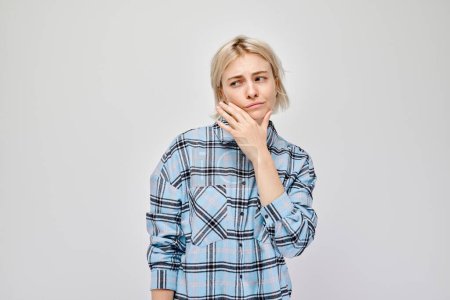 Photo for Thoughtful young woman with a hand on her chin, against a light grey background. - Royalty Free Image