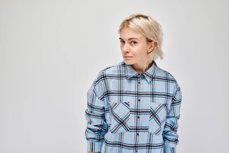 Téléchargez les photos : Portrait de jeune femme blonde portant une chemise à carreaux, regardant sur le côté sur un fond gris - en image libre de droit