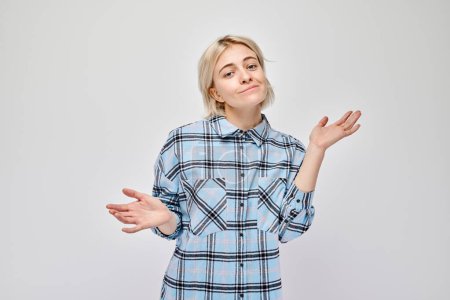 Photo for Confused young woman shrugging shoulders in plaid shirt against a gray background. - Royalty Free Image