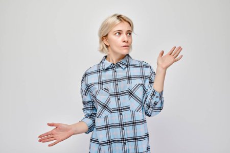 Photo for Confused young woman shrugging shoulders in plaid shirt against a gray background. - Royalty Free Image