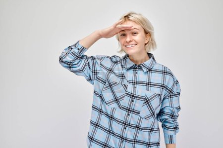 Téléchargez les photos : Femme souriante en chemise à carreaux saluant sur un fond gris - en image libre de droit