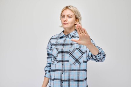 Foto de Mujer segura haciendo gestos para detenerse con la mano, señalando límites o rechazando sobre fondo gris. - Imagen libre de derechos