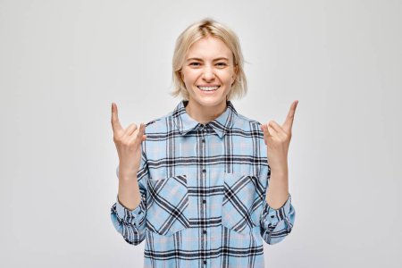 Téléchargez les photos : Joyeux jeune femme en chemise à carreaux faisant signe rock and roll, isolé sur fond gris. - en image libre de droit