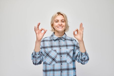 Téléchargez les photos : Femme souriante en chemise à carreaux faisant signe OK avec la main sur un fond clair. - en image libre de droit