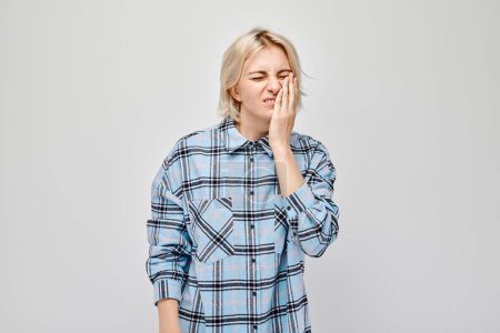 Photo for Portrait of woman looking stressed with hand on face, suffers from toothache - Royalty Free Image