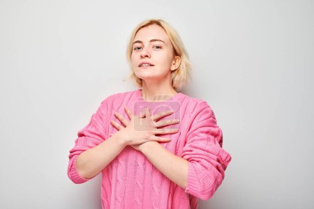 Téléchargez les photos : Femme en pull rose mains sur la poitrine exprimant gratitude ou sincérité isolé sur fond clair - en image libre de droit