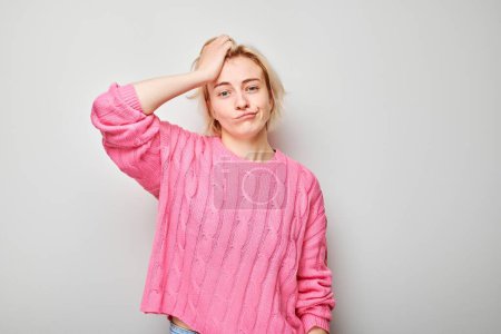 Téléchargez les photos : Jeune femme confus en pull rose se grattant la tête sur fond gris exprimant l'incertitude - en image libre de droit