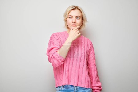 Photo for Young woman in pink sweater pondering over gray background. - Royalty Free Image